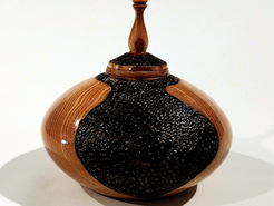 A stout, rounded wooden container with a delicately carved pointed top and inky black decorative texture.