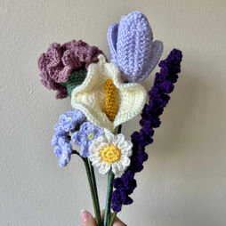 A hand holding a bouquet of various crocheted flowers.