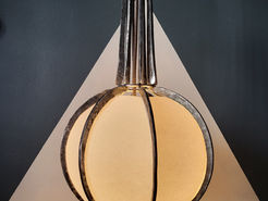 A forged metal lamp in the shape of a sphere and spire, its base illuminated.