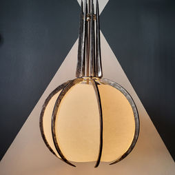 A forged metal lamp in the shape of a sphere and spire, its base illuminated.