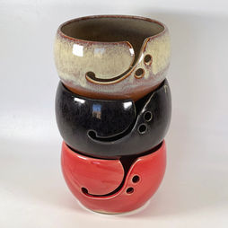 Three stacked pottery bowls in gray, black and red, decorated with curved openings shaped similarly to a bass clef.