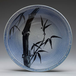 A round blue pottery dish with patterned edges and a black illustration of bamboo.