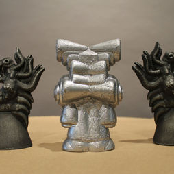 Three metallic sculptures of fantastical creatures facing in three different directions, in silver and black.