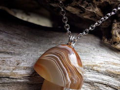 A polished brown gemstone in the shape of a mushroom, hanging from a silver chain against a wooden backdrop.