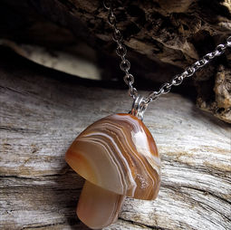 A polished brown gemstone in the shape of a mushroom, hanging from a silver chain against a wooden backdrop.