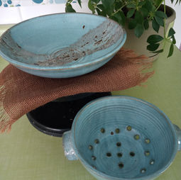 A light blue pottery bowl and colander, surrounded by everyday home decor.