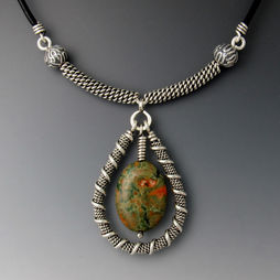 An oval shaped green and orange stone surrounded by teardrop-shaped metal coil, hanging from a spiral metal chain.