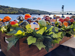 A diverse selection of small patterned glass mushrooms, inside a wooden planter box filled with ivy.