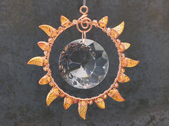 A jeweled copper suncatcher in the shape of the sun, with transparent orange leaves as rays.