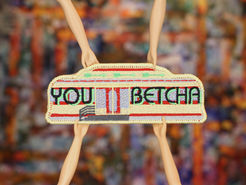 A patch in the shape of a diner car reading, "You Betcha," held by four doll hands.