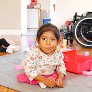 Young child sits on floor with toys and wheelchair in background