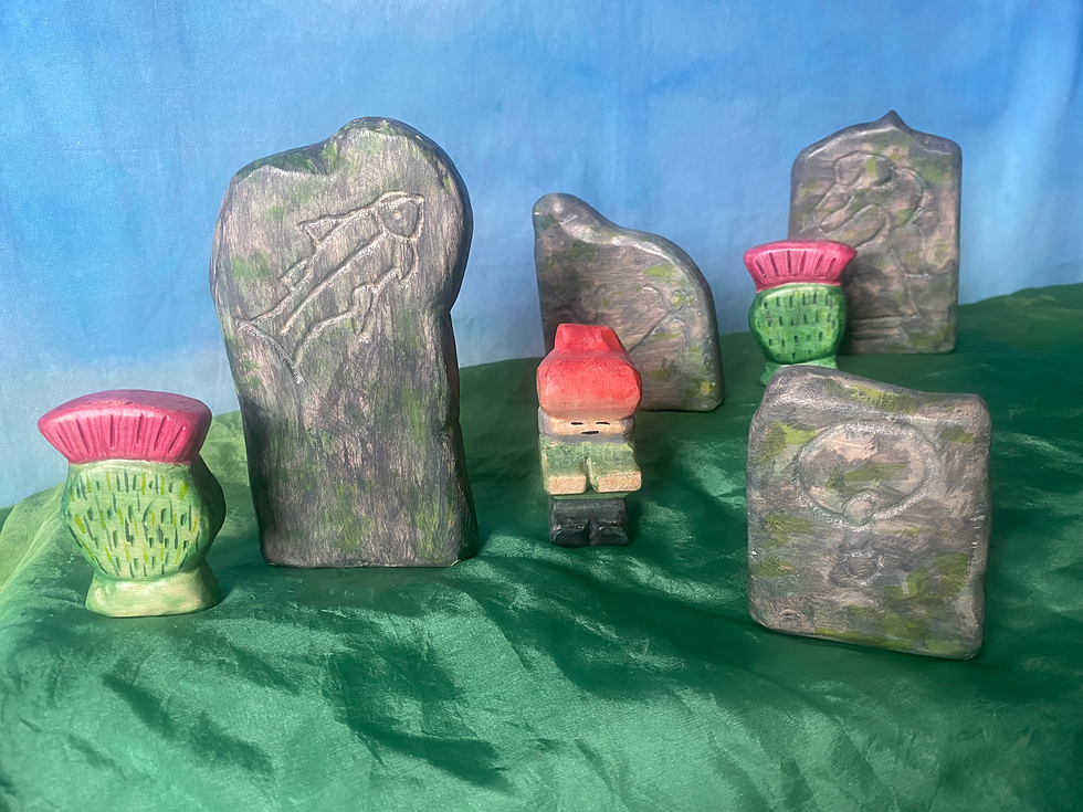 image shows a selection of painted wooden toys including a small figure, carved standing stones and pink thistles