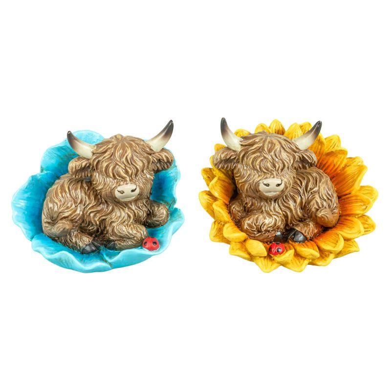 two highland cow figurines resting on flowers, one blue and one yellow