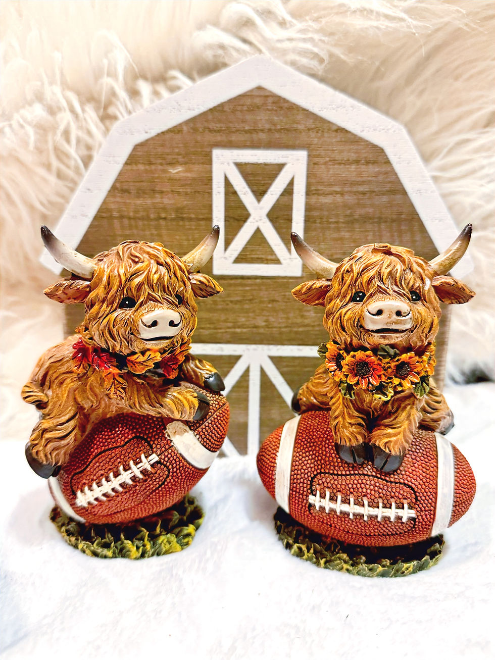 Highland cow figurines with floral garlands sitting on footballs, rustic fall farmhouse décor for sports and autumn fans.