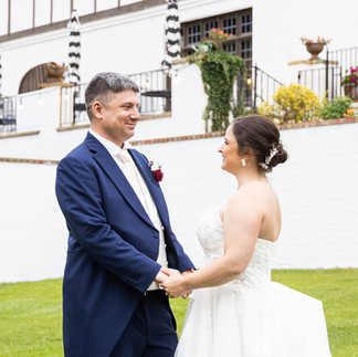 Bride and groom holding hands during an outdoor wedding at a historic estate venue, sharing a joyful moment surrounded by elegant architecture and landscaped grounds.