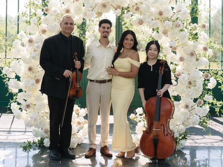 Proposal musicians at The Little Chapel at Haven Ridge in Winston-Salem NC with violin and cello duo standing beside engaged couple beneath a floral arch inside the Solarium
