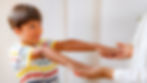 Young boy in a striped shirt reaches his hands to an adult’s open palms, smiling softly in a bright, airy room.