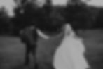 Bride and groom walking hand in hand in a field.