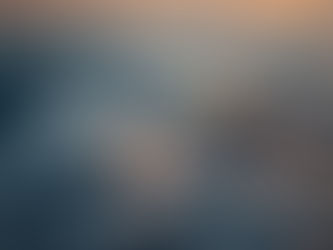 Snow-capped mountain peak emerging through clouds at sunset, with warm orange and pink hues highlighting the dramatic sky above.