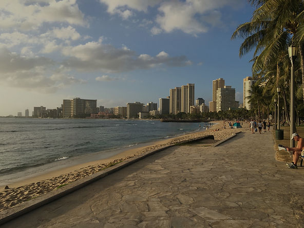 Walking Downtown on Waikiki Beach shoreline with palm trees, sandy path, and Honolulu city skyline at sunset, Oahu, Hawaii