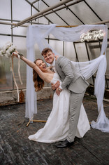 Brautpaar vor dem Traubogen beim Brautpaarshooting, die Braut hebt den Strauß hoch, der Bräutigam hält die Braut im Arm