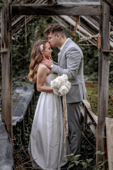 Brautpaarshooting mit dem Brautpaar, welches im Gang eines alten, verwilderten Gewächshauses steht, der Bräutigam küsst die Braut auf die Stirn