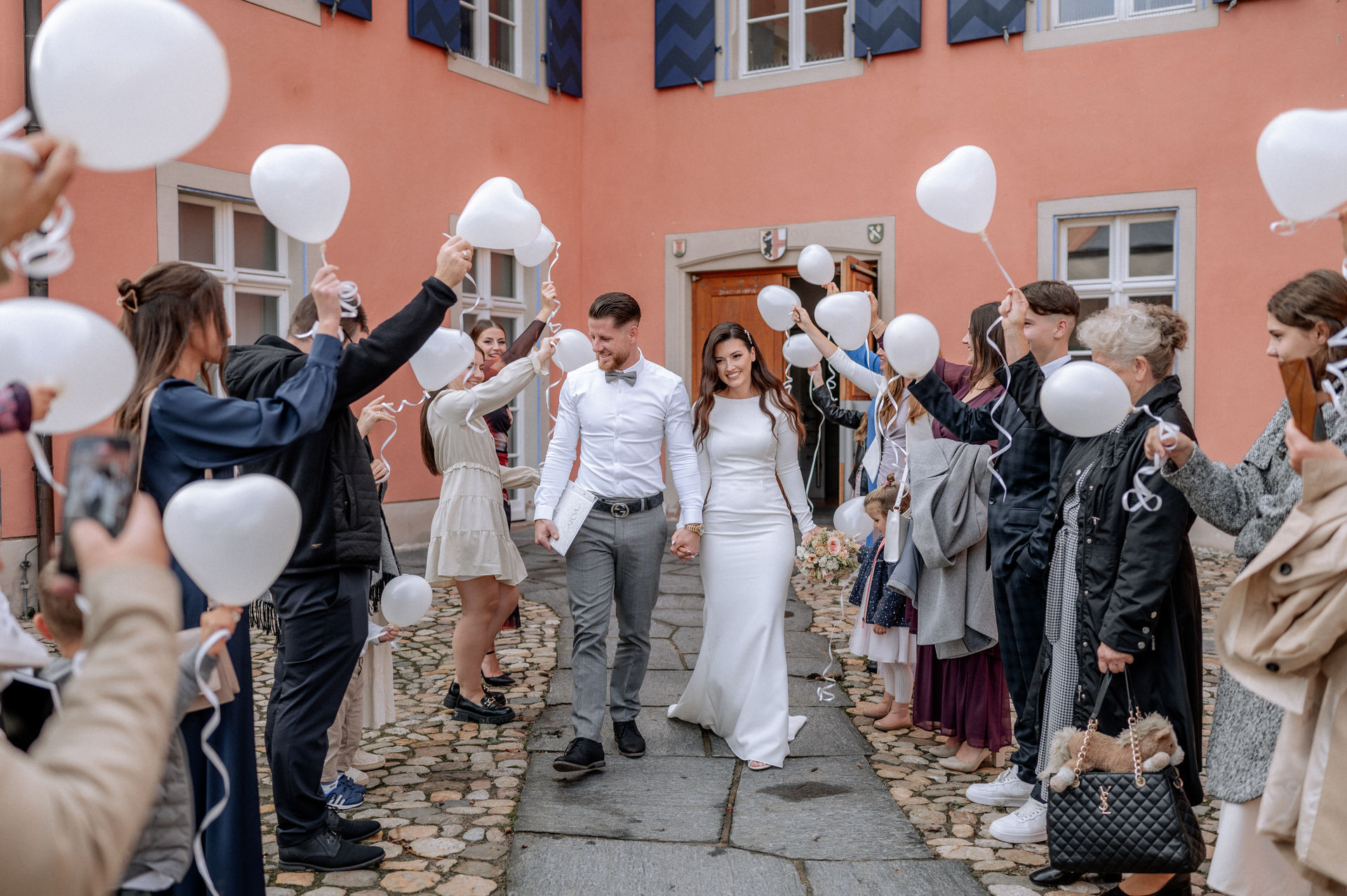 das Brautpaar, das durch den Spalier der Gratulanten mit Luftballons läuft