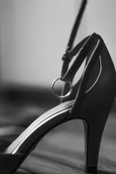 Ehering hängt symbolisch am Riemchen eines eleganten Brautschuhs