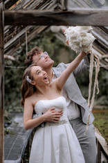 Das Brautpaar beim Brautpaarshooting, der Bräutigam steht hinter der Braut und diese hält den Strauß in die Höhe und lacht dabei