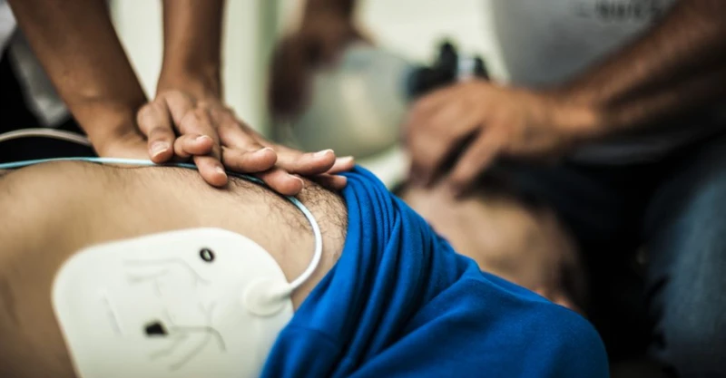 Person preforming CPR on a patient or victim. Defibrillator pads applied on victim's chest wall