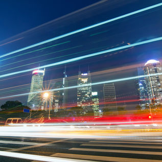 Shanghai's Pudong financial district at night, with illuminated skyscrapers and streaks of light from traffic across the sky