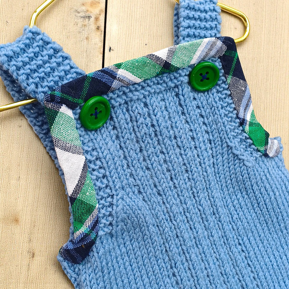 Close-up of front bib on pale blue merino wool baby dungarees with green and navy tartan trim and green wooden buttons