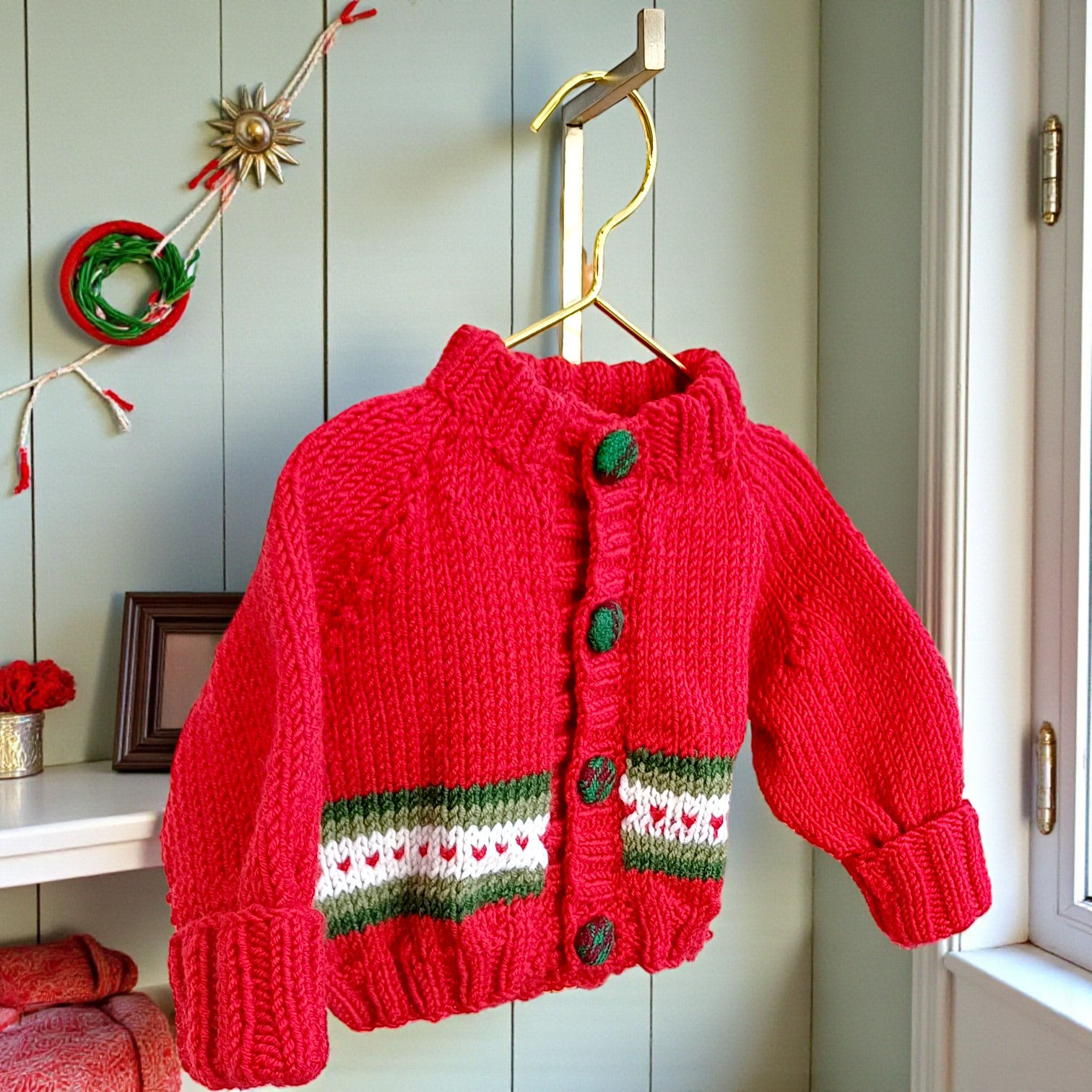 Red merino wool newborn cardigan with tartan-covered buttons and heart stripe detail.