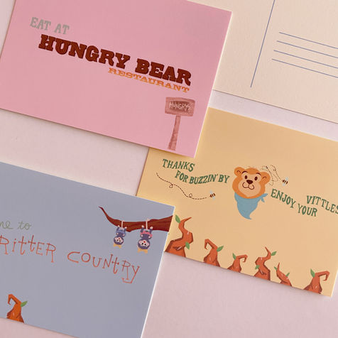 Set of 3 postcards inspired by the hungry bear restaurant inside of Disneyland in critter country one is pink and says eat at hungry bear and a yellow one with a bear that says enjoy your vittles and a blue one that says welcome to critter country