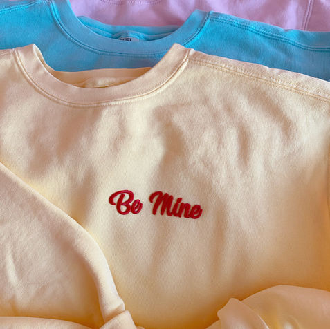 5 pastel color crewneck sweaters: yellow, pink, teal, blue and purple. With the phrase from the Candy Hearts ‘be mine’ embroidered in red thread 