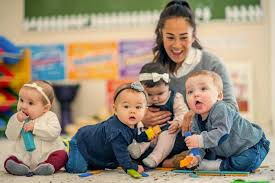 Smiling caregiver with four babies playing on the floor
