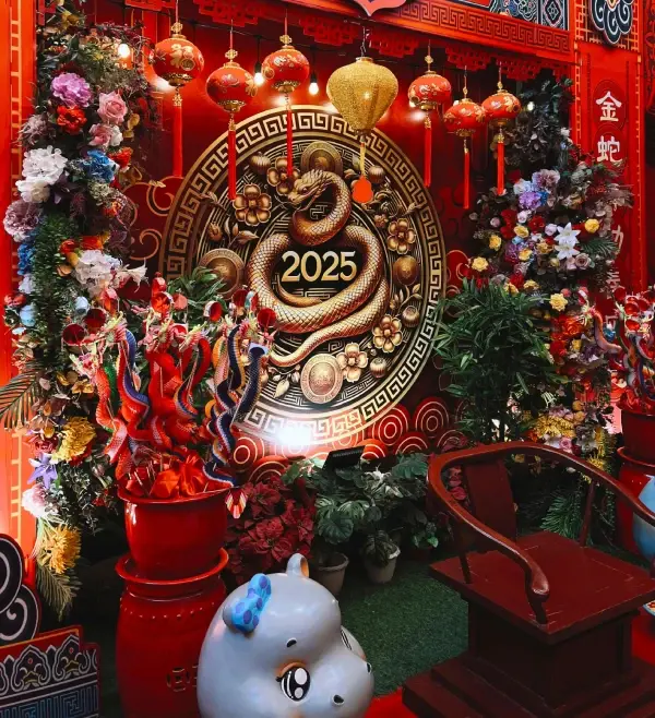 Red and gold Chinese New Year display with a snake motif, "2025" text, lanterns, flowers, and a colorful dragon decoration. Festive atmosphere.