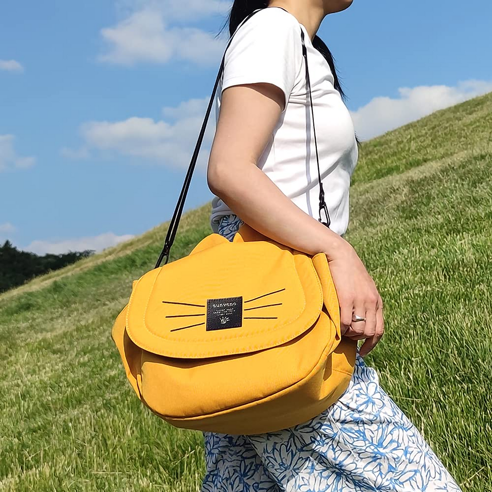Woman carrying a yellow cat-shaped shoulder bag on a grassy hill.