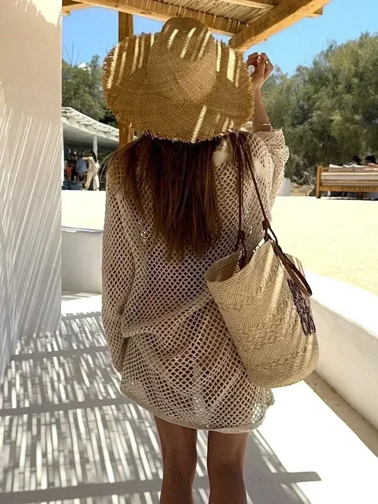 Woman in mesh cover-up and straw hat at beach club.