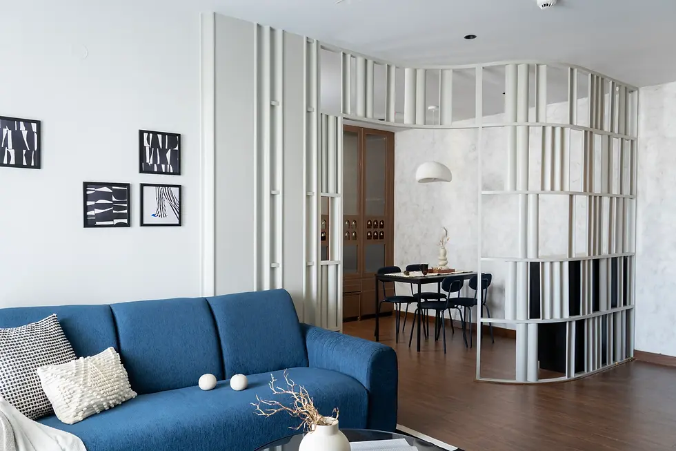 Modern living room with a blue sofa, minimalist decor, and a white vertical slat partition separating the dining area.