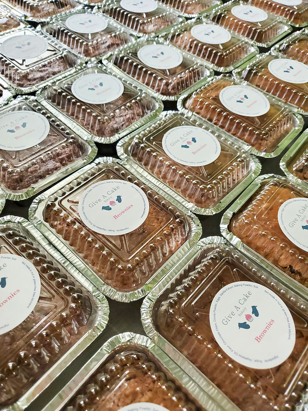 Rows of individually packaged brownies in aluminum containers with “Give A Cake Bakery” labels, neatly arranged and ready for community delivery.
