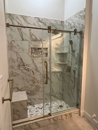 Gold calacatta shower tile. Glass door. Pebble stone floor.