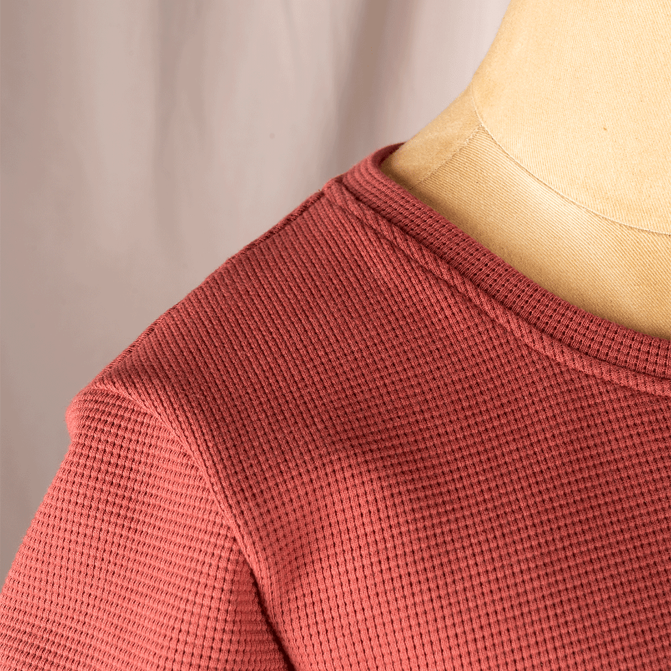 Detail vom Rundhalsausschnit von einem roten Waffelstrickpullover.
