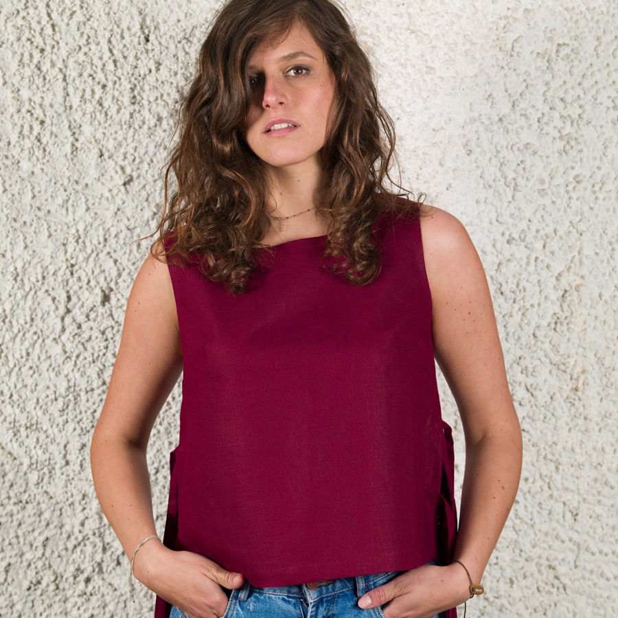 Miniaturbild: Braunhaarige Frau mit Locken trägt eine weinrote Leinenbluse über einer blauen Jeans.
