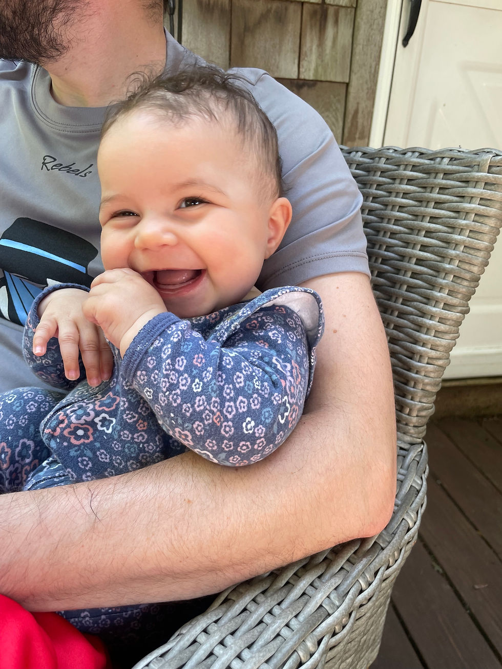 A baby is sitting on an adult's lap, smiling and looking around. The baby is not engaged in a specific activity, representing unoccupied play.
