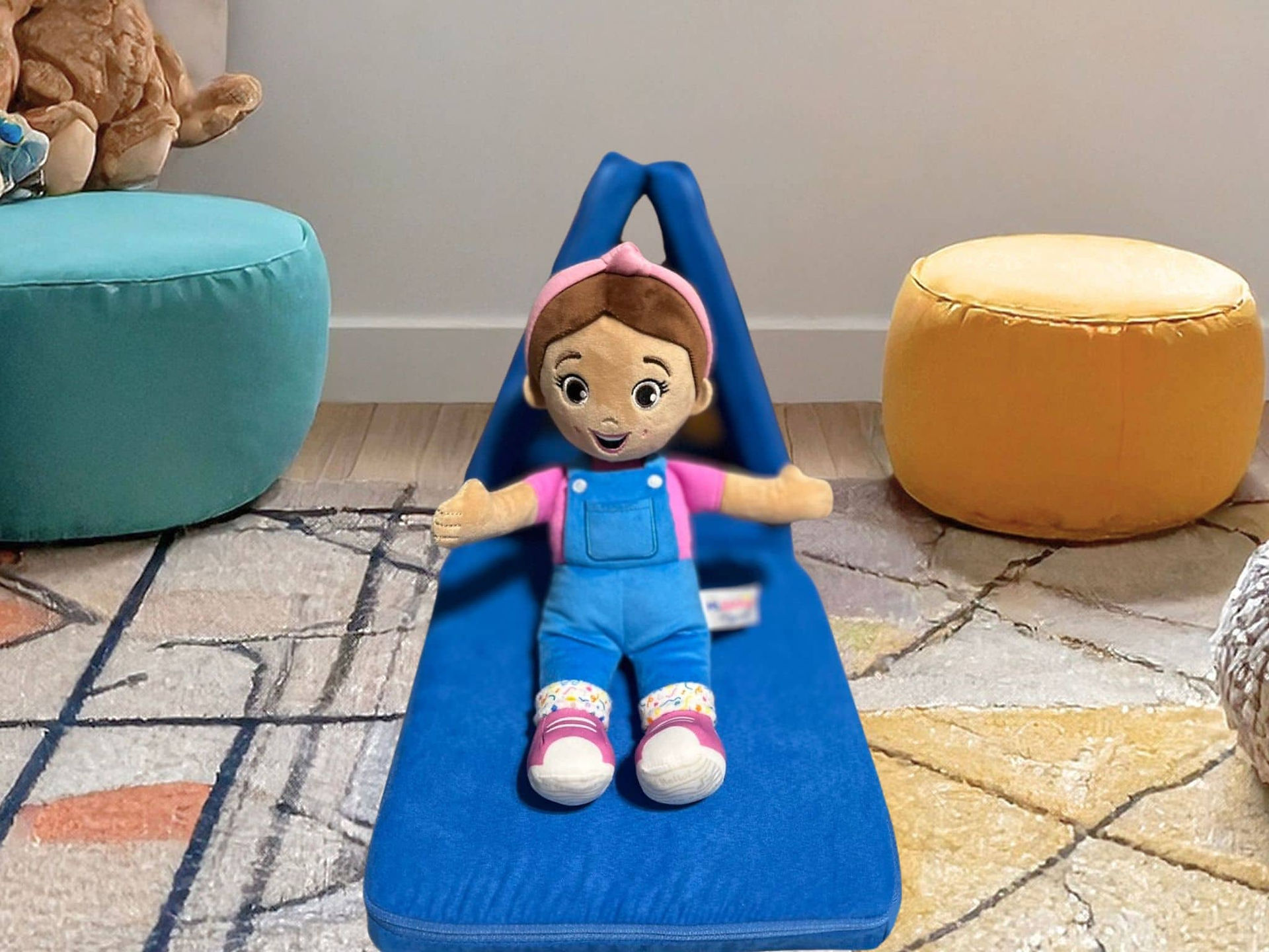 Plush Ms. Rachel doll sits on a Mini Nugget build. Background is the carpet of a playroom in between two poufs.