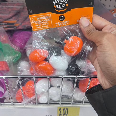 A hand holds a package of Hyde and Eek! Boutique Halloween squishy toys at Target. The bag contains 12 small pumpkin- and ghost-shaped squishies in orange, white, and black The set is priced at $3 on the shelf.