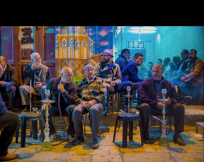 Men sitting outside a cafe with hookahs at night.