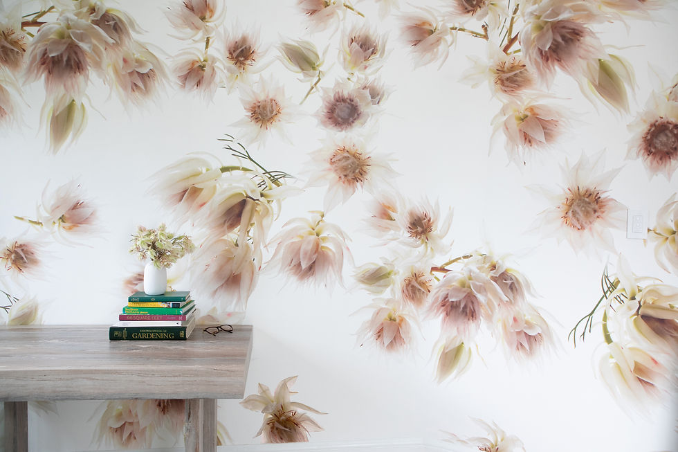 A table with books and a vase with flowers against a large scale pink floral wallpaper. Soft pinks and greens create a tranquil, elegant setting.