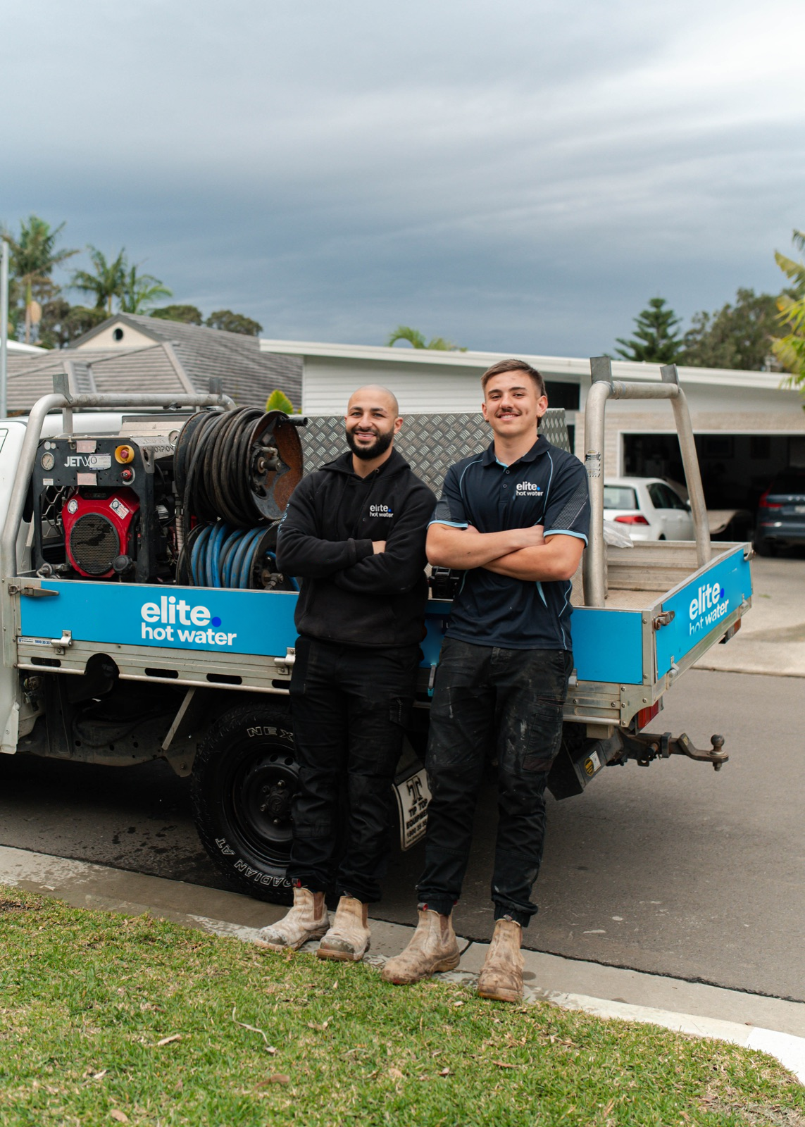 Two Elite Hot Water team members beside a branded service vehicle
